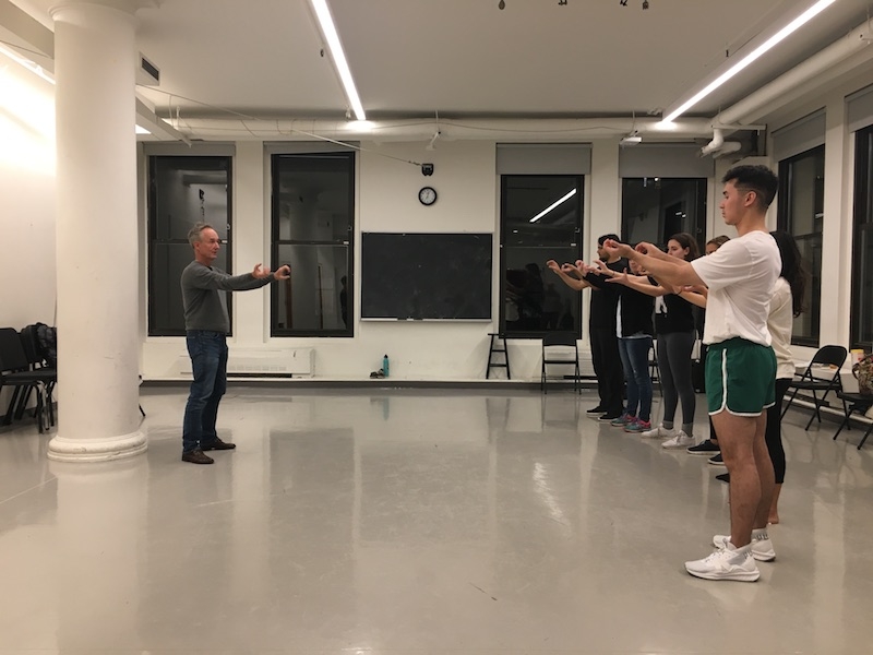 Jacob Oleson holding his arms like he is holding a stick, leading a miming exercise with the workshop attendees.